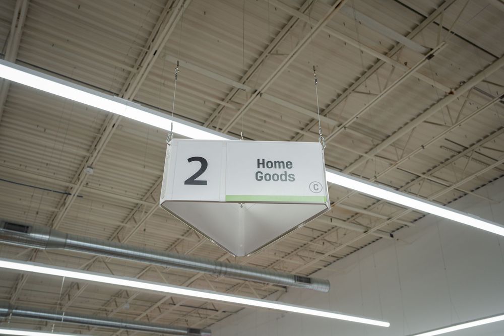 Store aisle signs and lighting fixtures hang from a white ceiling in a retail environment.