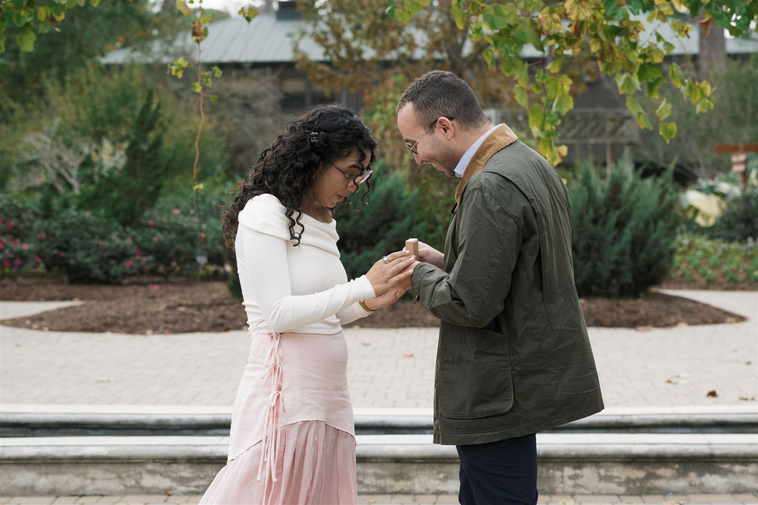 A couple in formal attire shares a tender moment in a garden setting during an outdoor photo session.