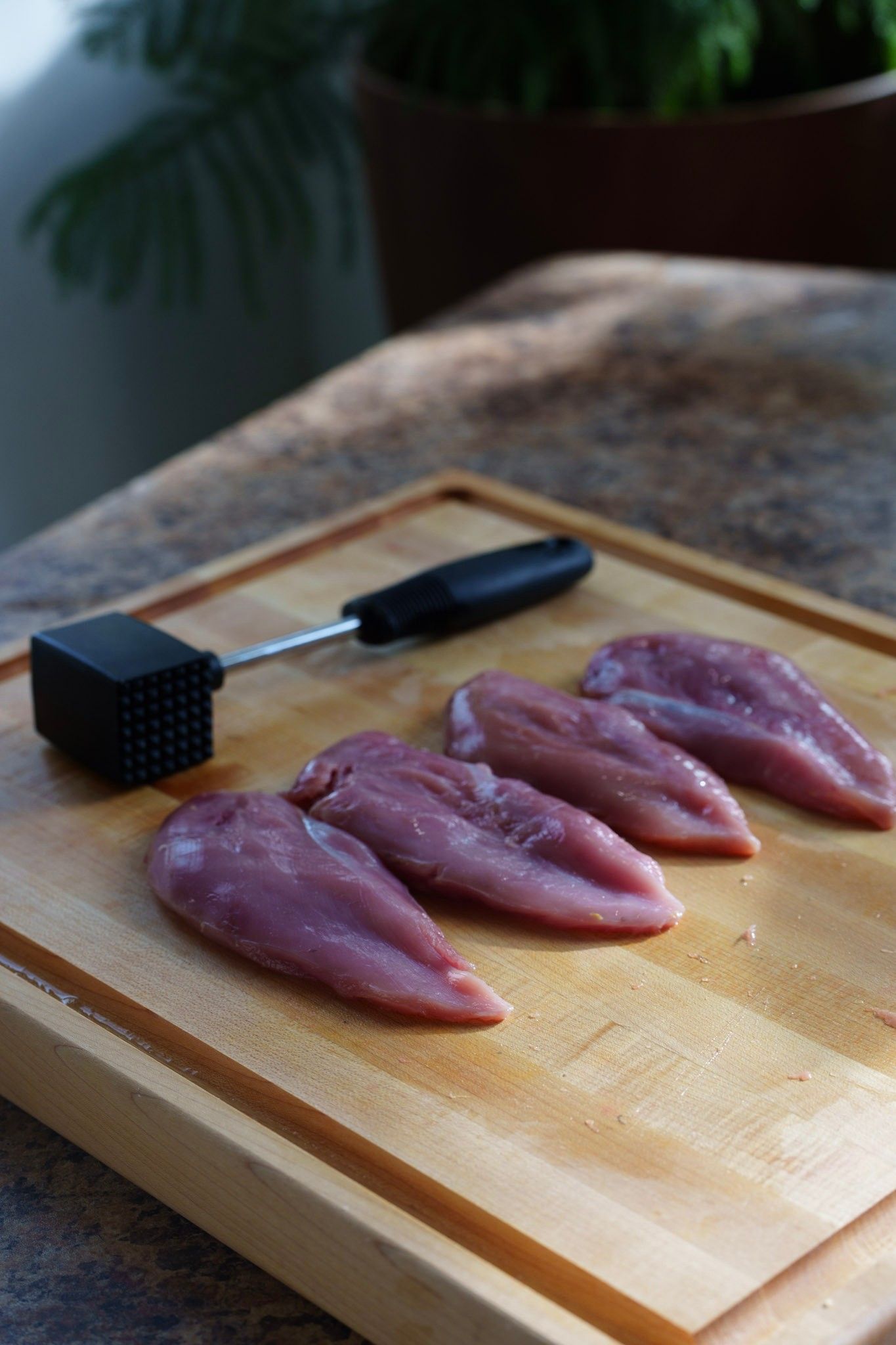 Raw chicken breasts being prepared on a wooden cutting board with a black knife.