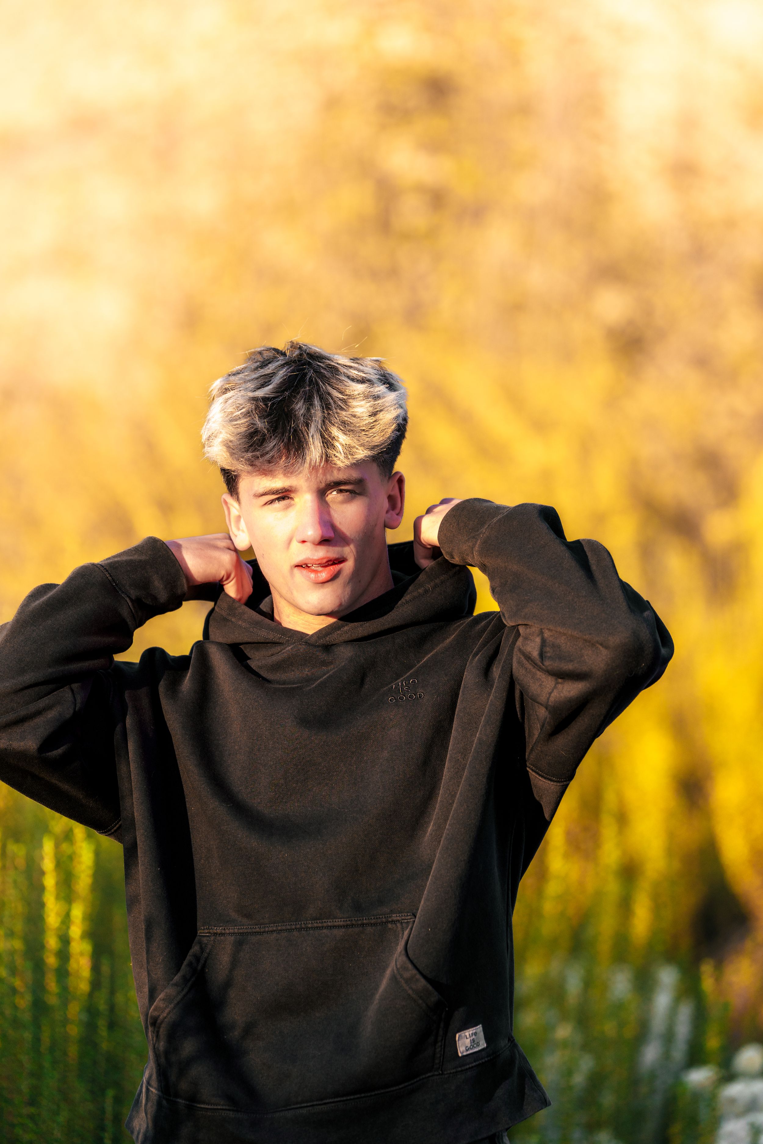Person in black hoodie posing against golden autumn background at sunset.