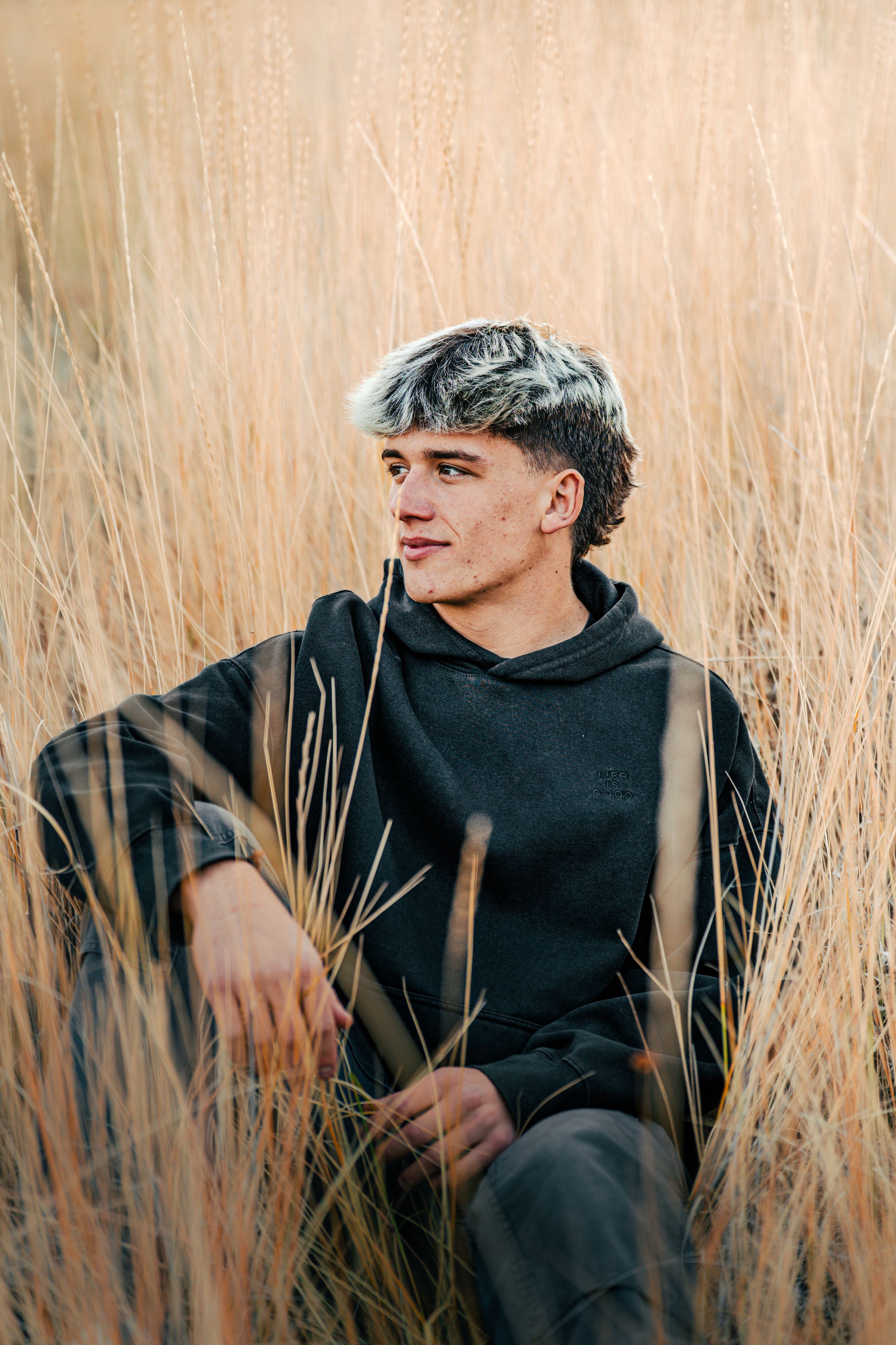 Artistic portrait through tall beige grass of person wearing dark hoodie.