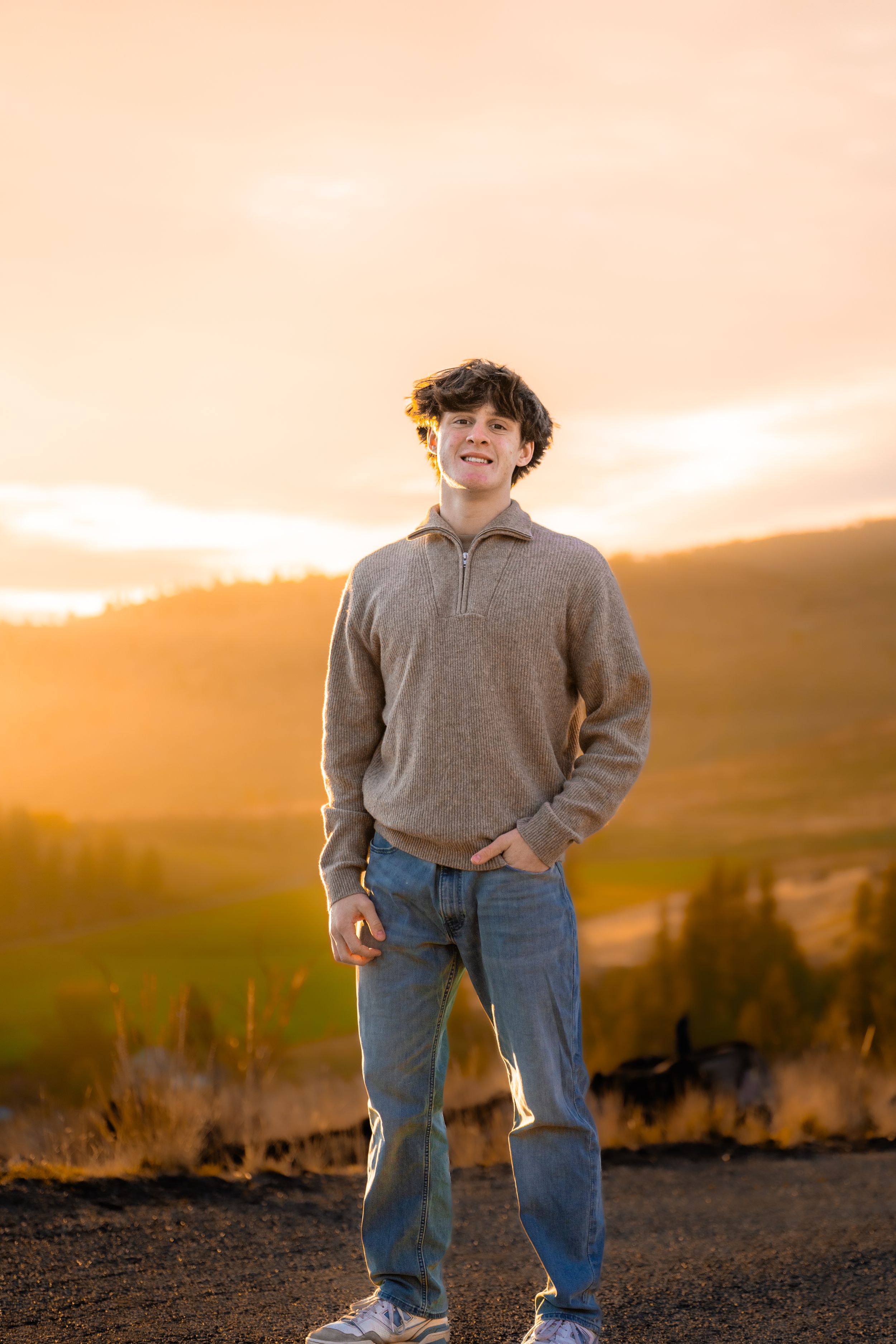 Figure in casual wear standing on hillside during golden sunset with mountains in background.