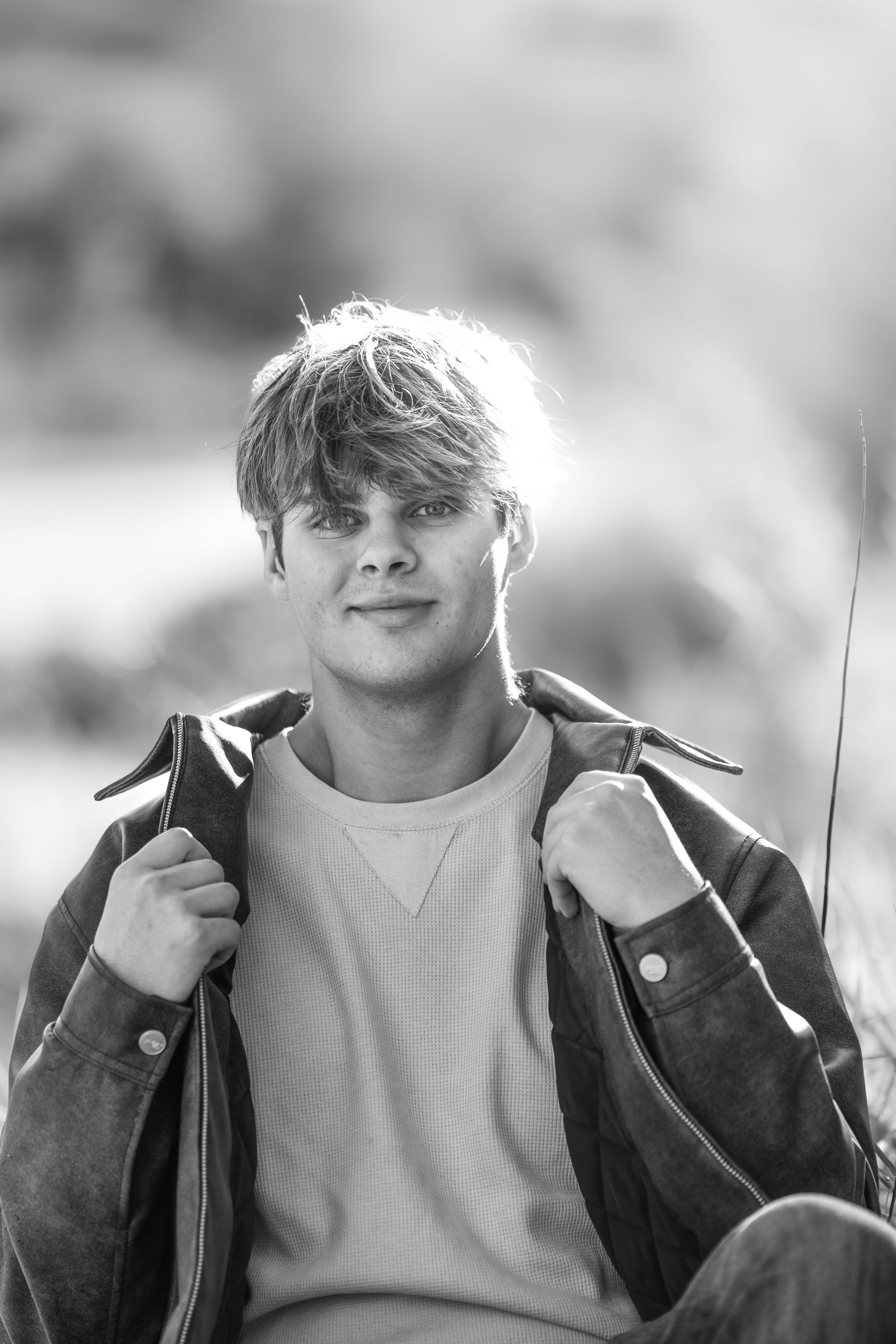 Close-up black and white portrait of person wearing brown jacket against blurred background.