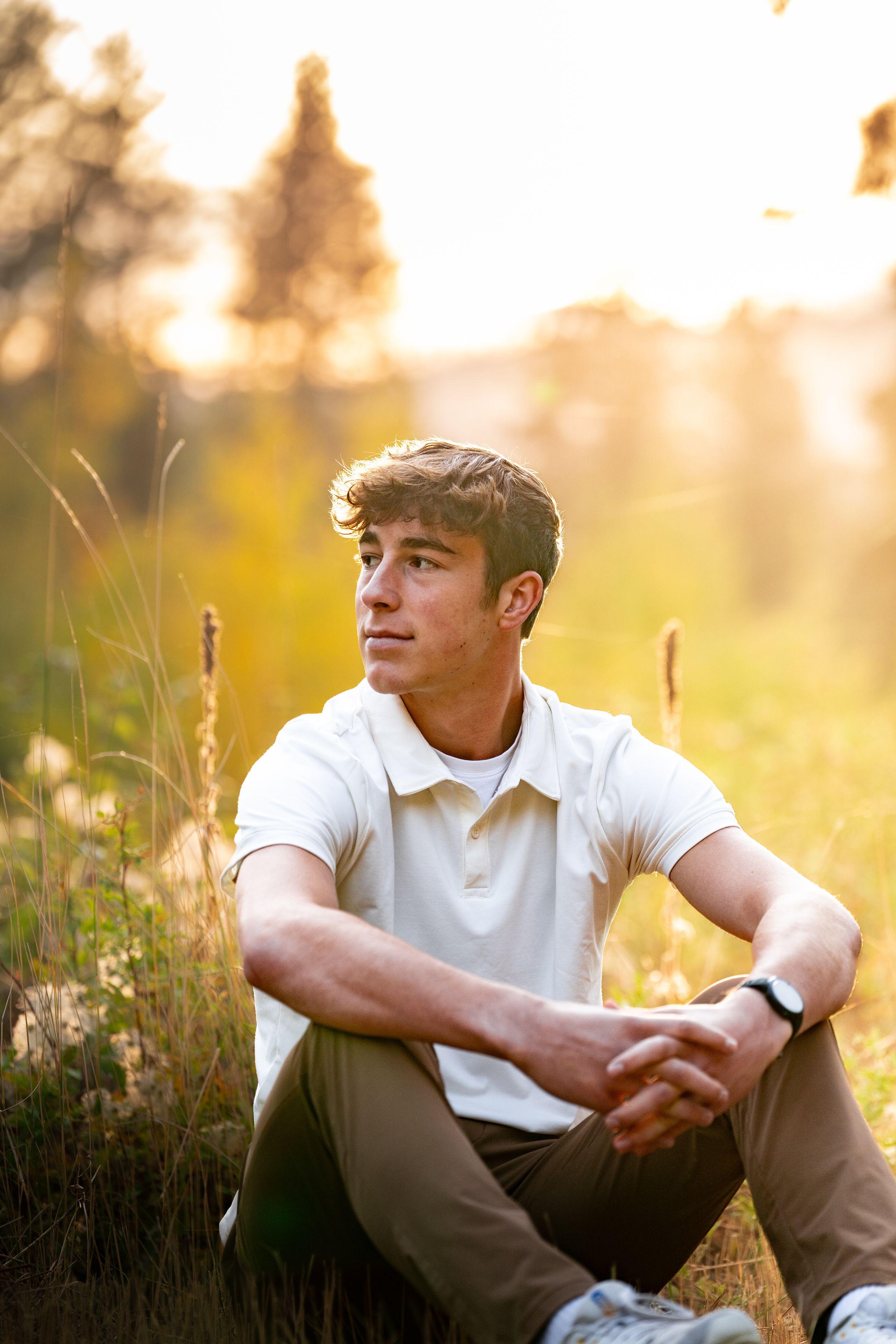 Person in white polo shirt sitting in sunlit meadow during golden hour.