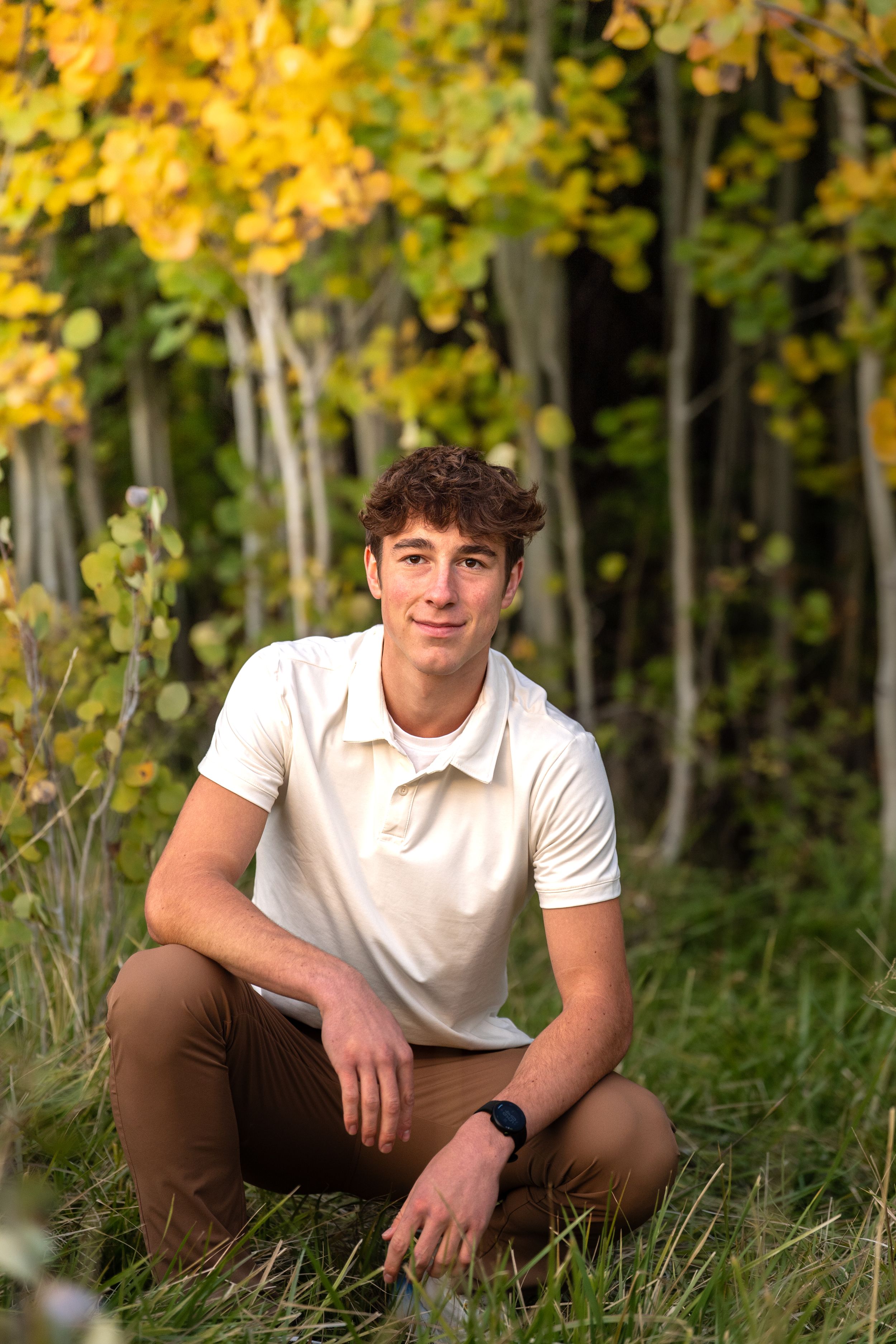 Athletic figure in white polo relaxing among yellow aspen trees in autumn setting.