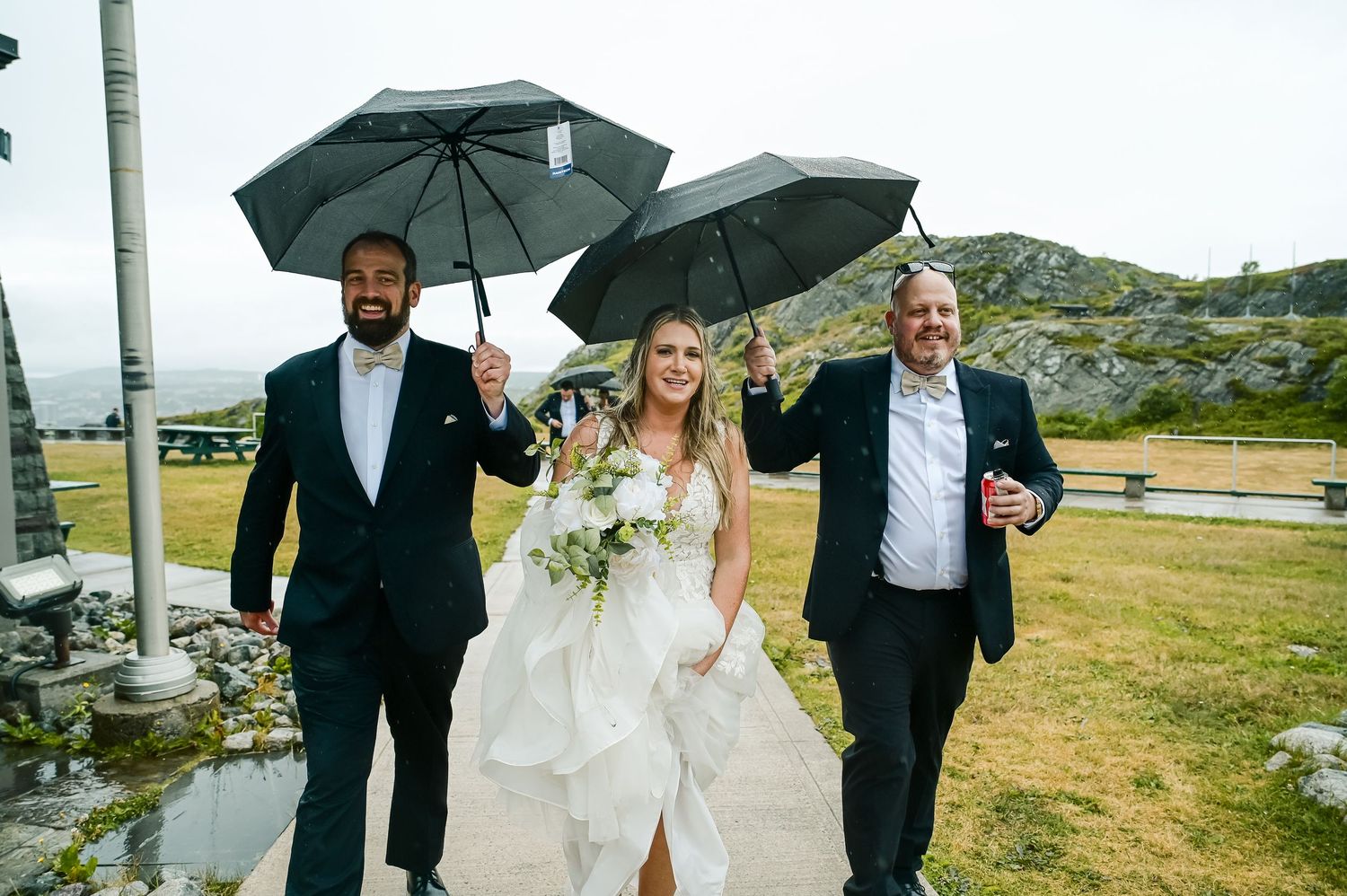 Bride covered by umbrellas on a rainy day, with everyone smiling and having fun.