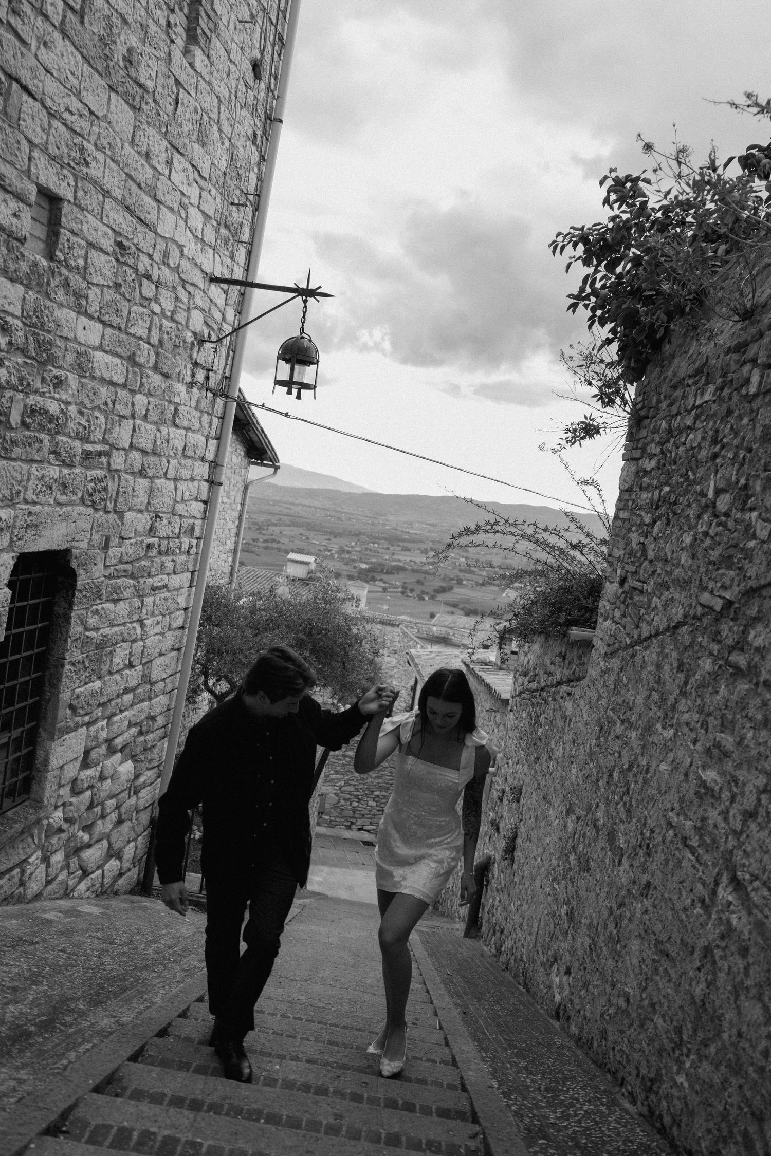 Black and white sequence of people walking down stone steps in a medieval village setting.