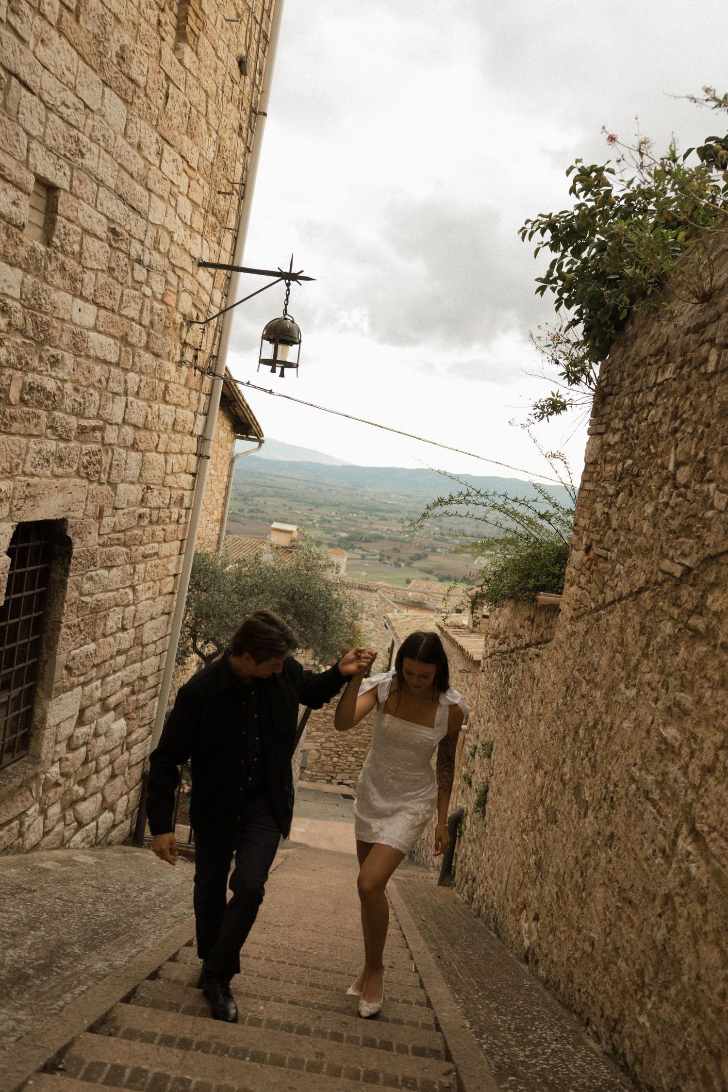 Two people descend stone steps in a medieval village on a cloudy day.