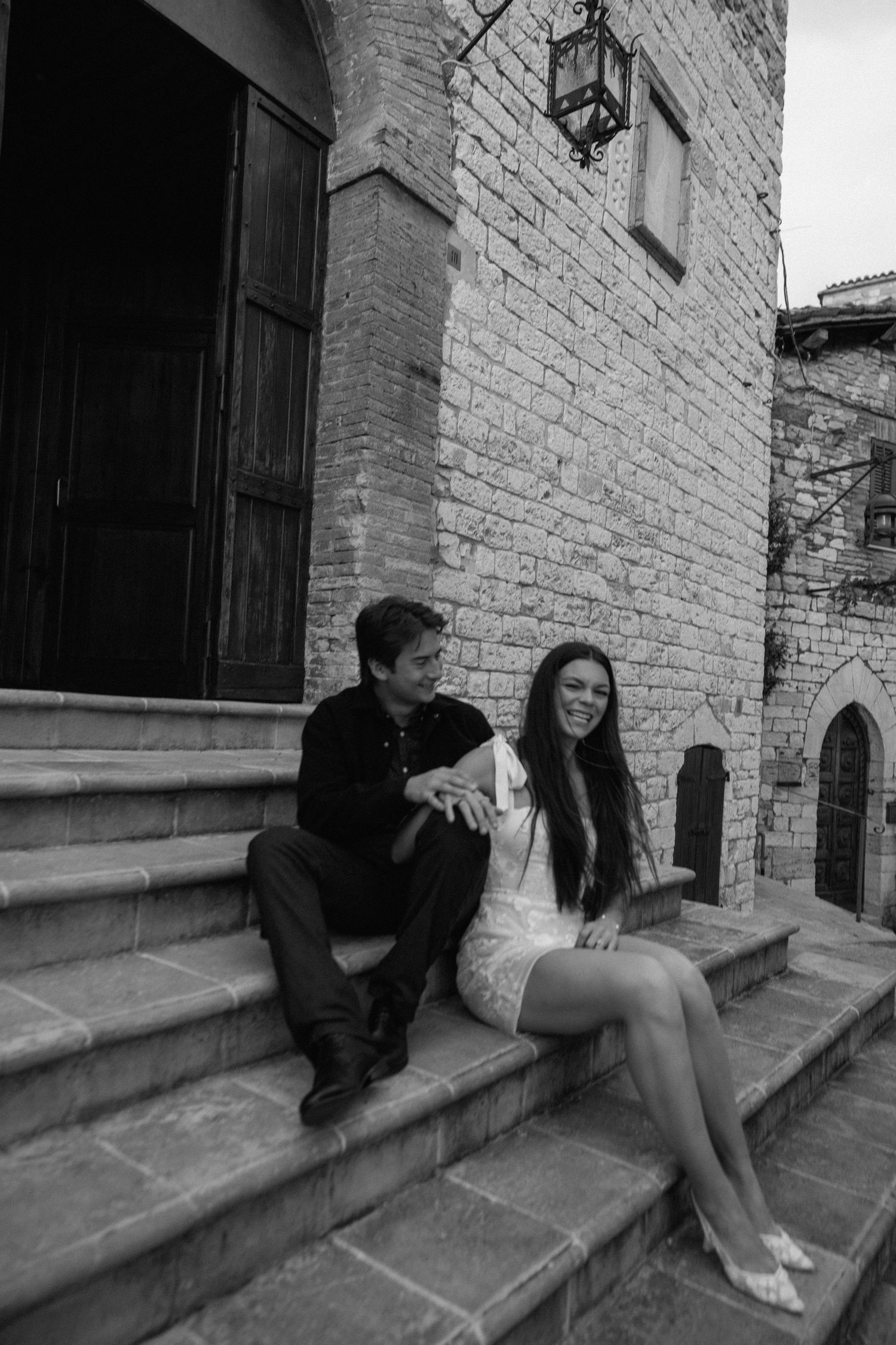 A couple sits together on stone steps outside a brick building in a series of candid black and white photos.