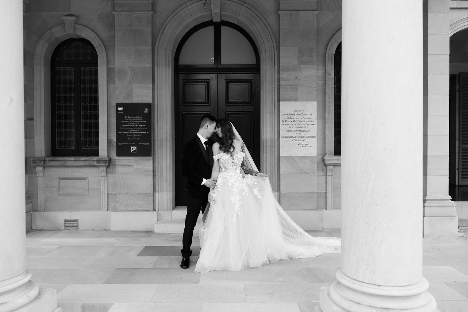 A couple embraces in a dimly lit colonnade with dramatic shadows and light streaming between classical columns.