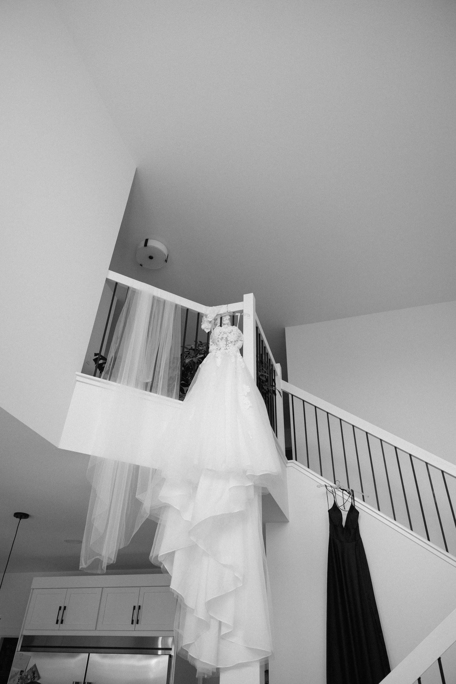 A white wedding dress hangs elegantly against a gray wall in natural light.