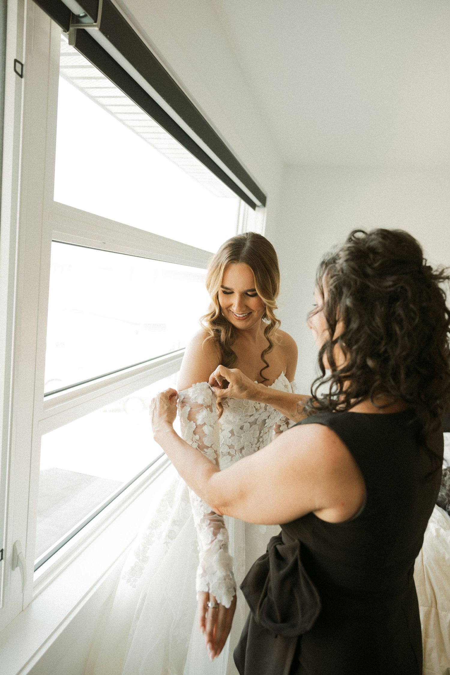 Behind the scenes photo shoot in bright white room with window light and photographer capturing model in dress.