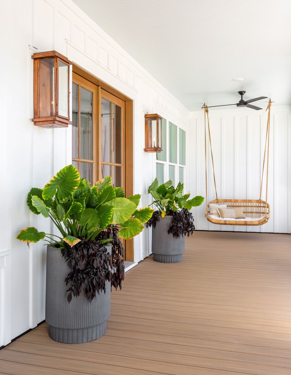 Modern porch with wooden deck flooring and large potted plants against white walls and copper lanterns.