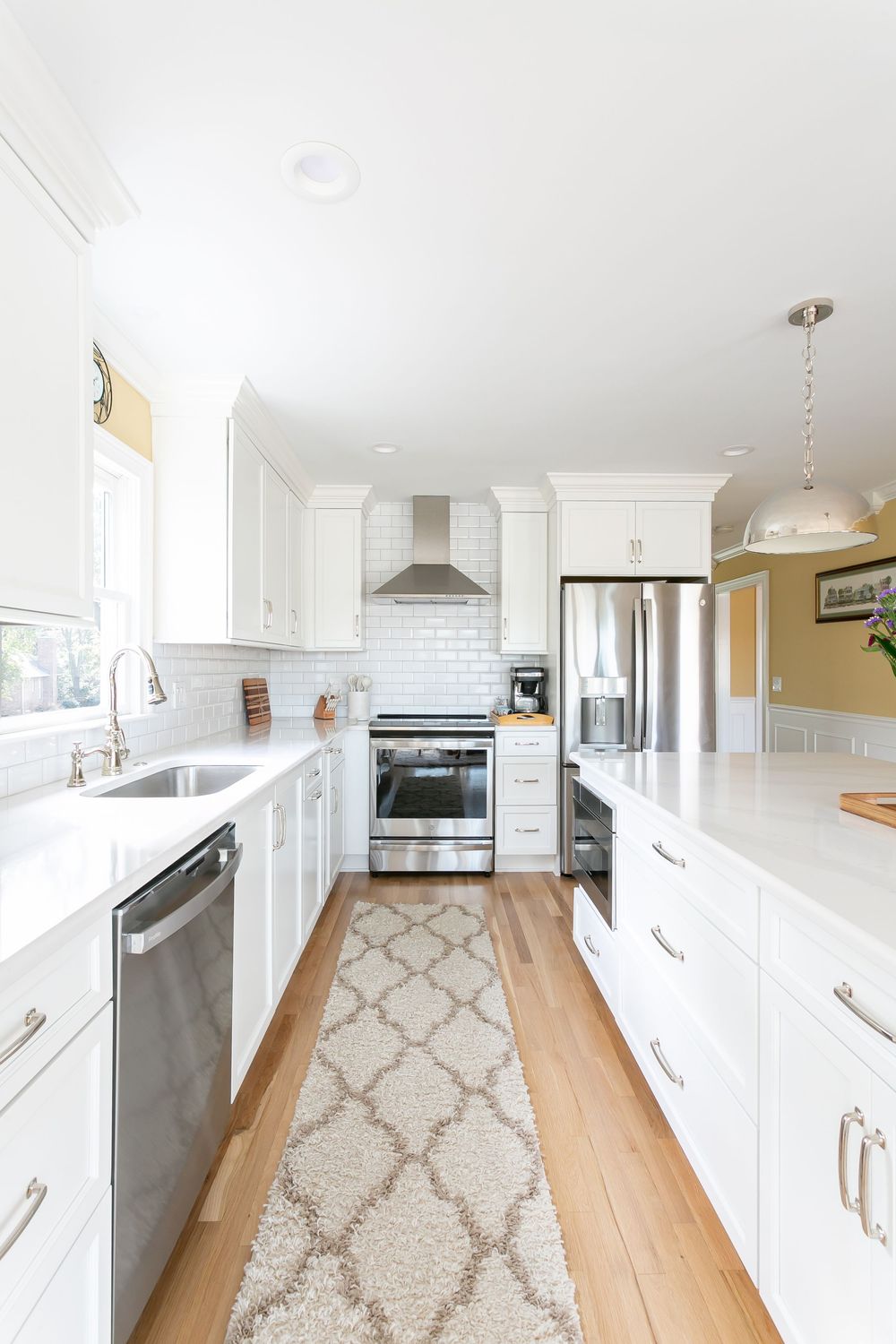 Bright white kitchen with light wood floors and a geometric pattern area rug.
