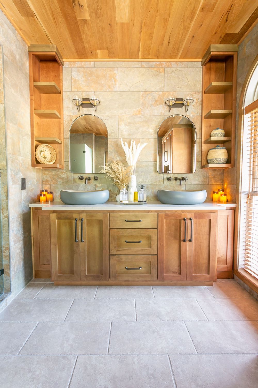 Rustic bathroom with wooden ceiling, stone walls, and dual vanity featuring warm lighting.