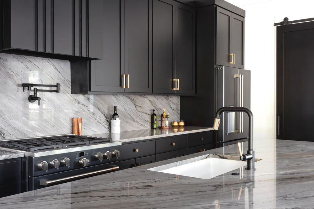 Modern black kitchen cabinets with marble backsplash and sleek stainless steel appliances.