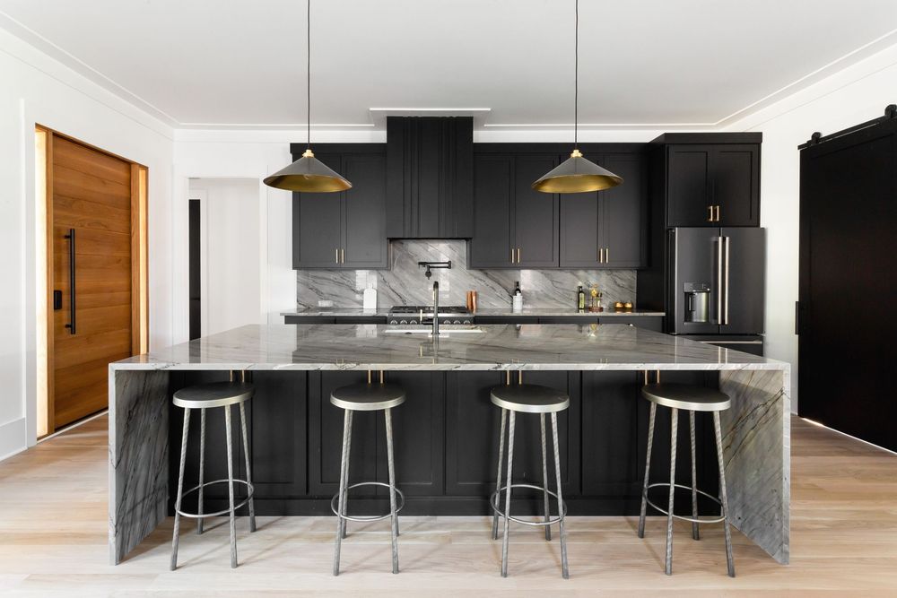Sleek black kitchen with waterfall island, modern bar stools, and pendant lighting.