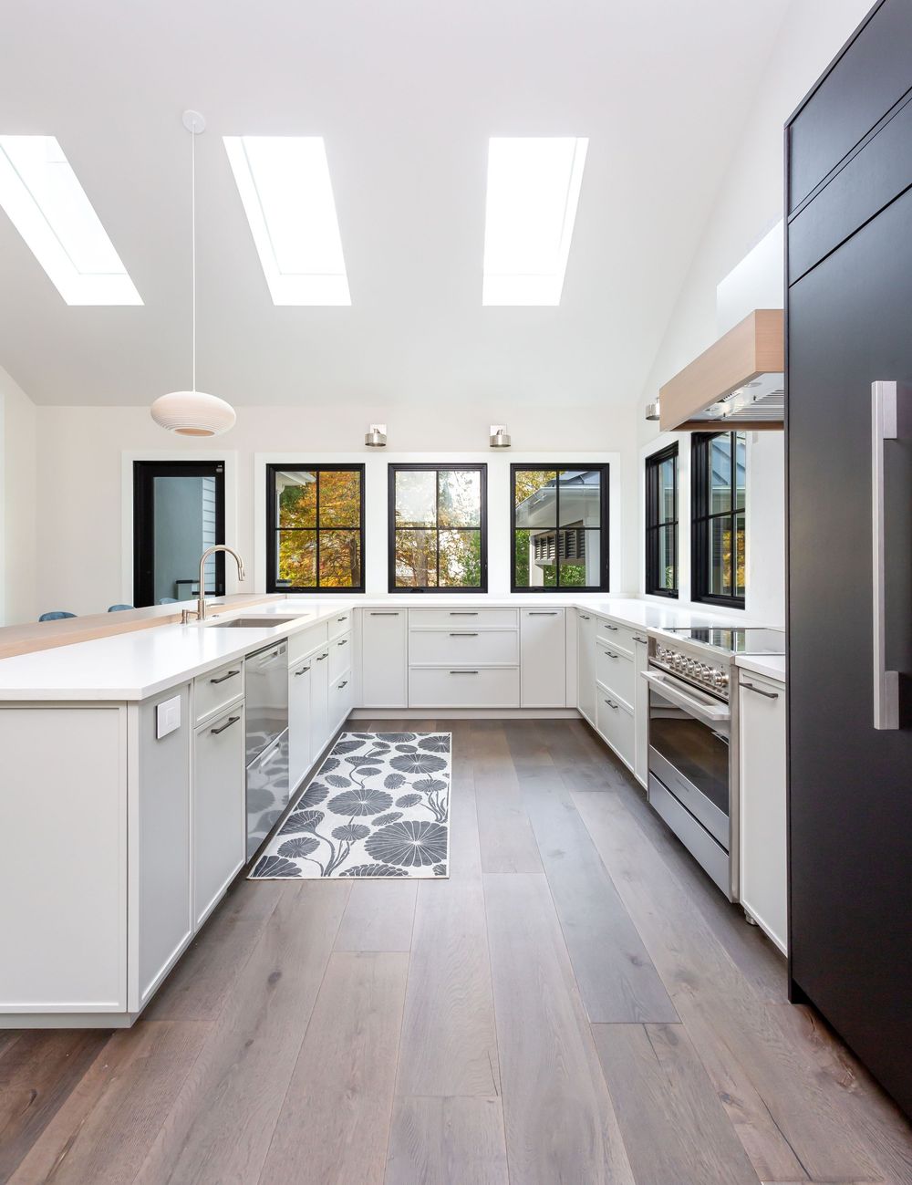 Bright modern kitchen with white cabinets, light wood floors, and large skylights.