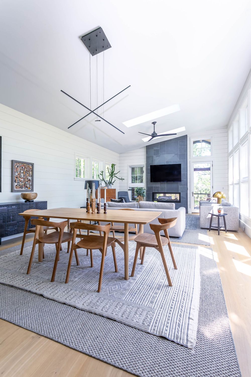 Bright dining area with wooden table, geometric rug, and vaulted ceiling with modern lighting.