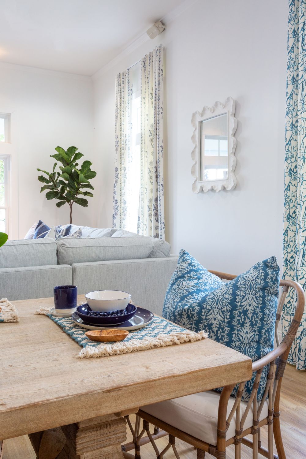 Dining room featuring a rustic wood table, blue floral curtains, and white walls.