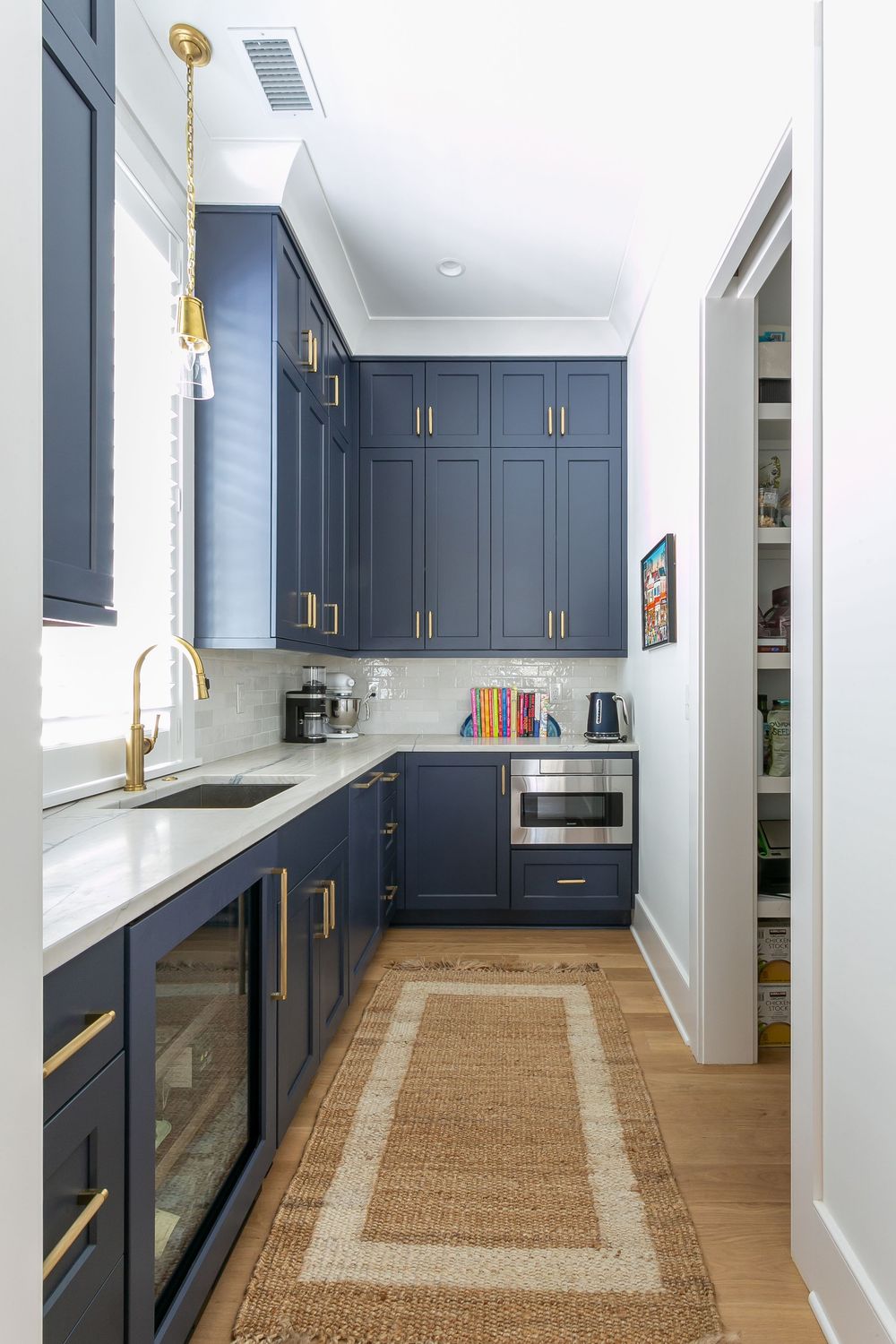 Navy blue galley kitchen with brass hardware and natural jute runner on hardwood floors.