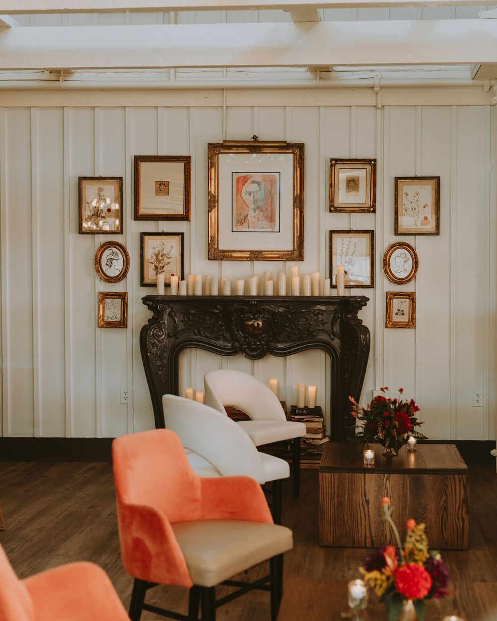 Vintage-style lounge area with coral chairs and framed artwork on white paneled walls.