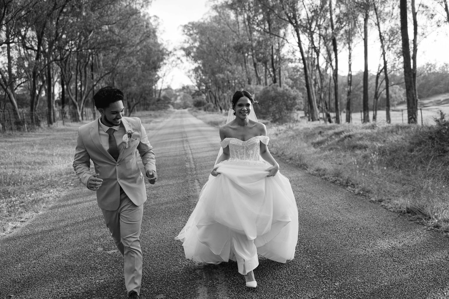 A romantic black and white photo series showing a couple walking hand in hand through a tree-lined path in wedding attire.