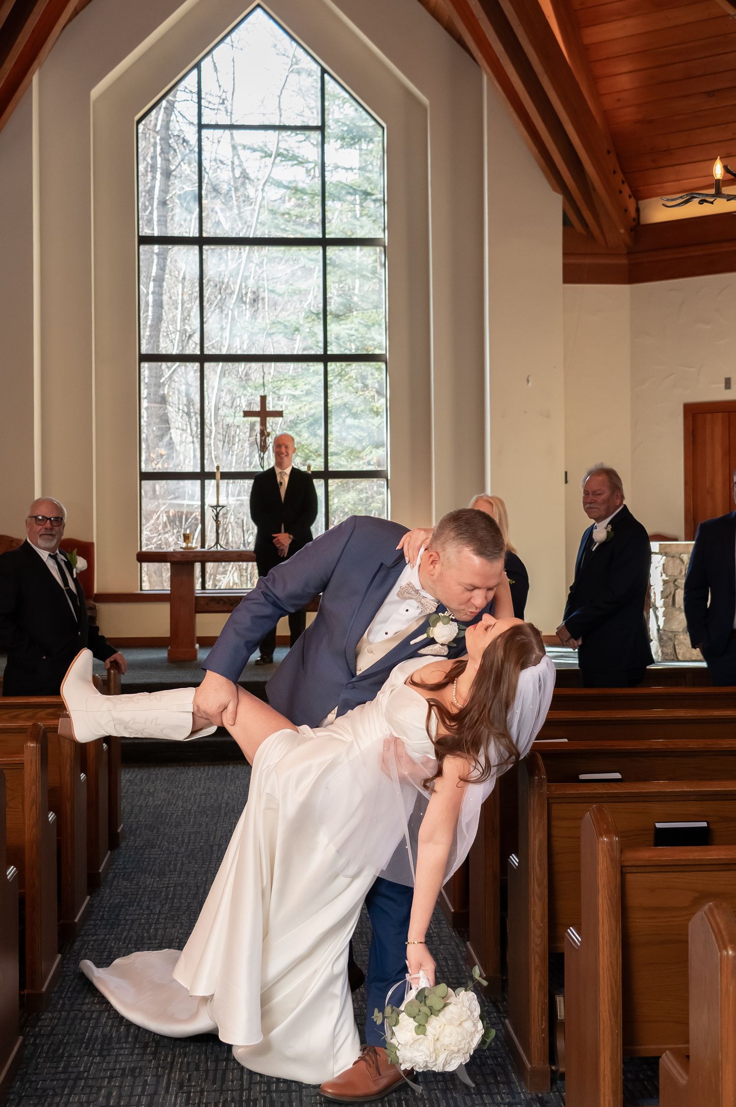 A couple performs a romantic dip during their wedding ceremony in a rustic wooden chapel with tall windows in The Beaver Creek Chapel