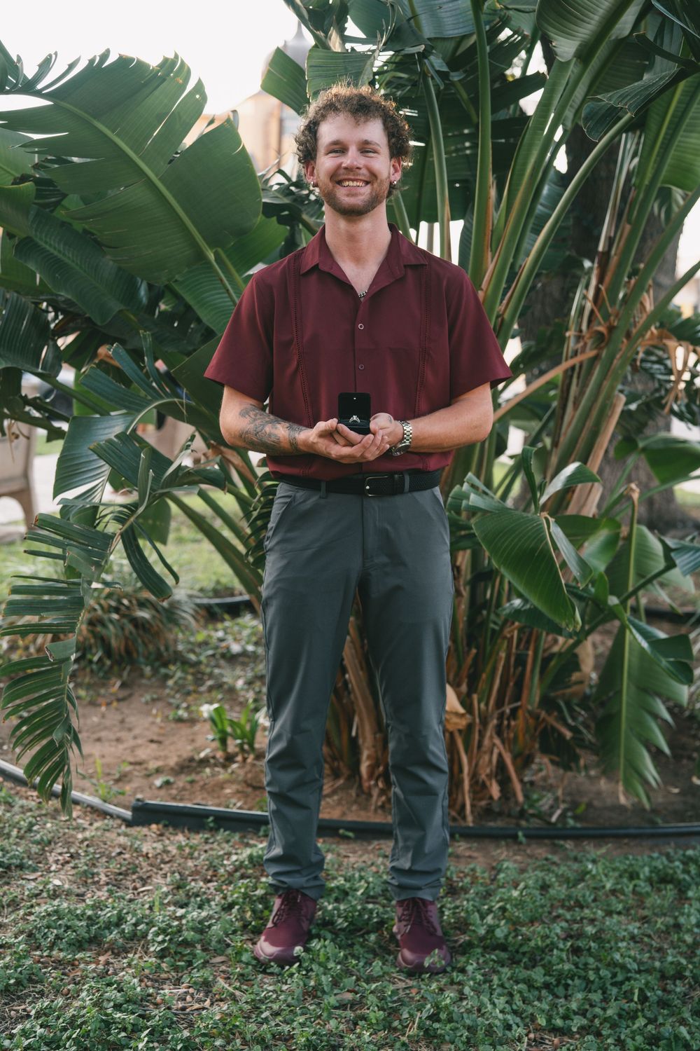 A couple stands in front of tropical plants during a proposal moment.