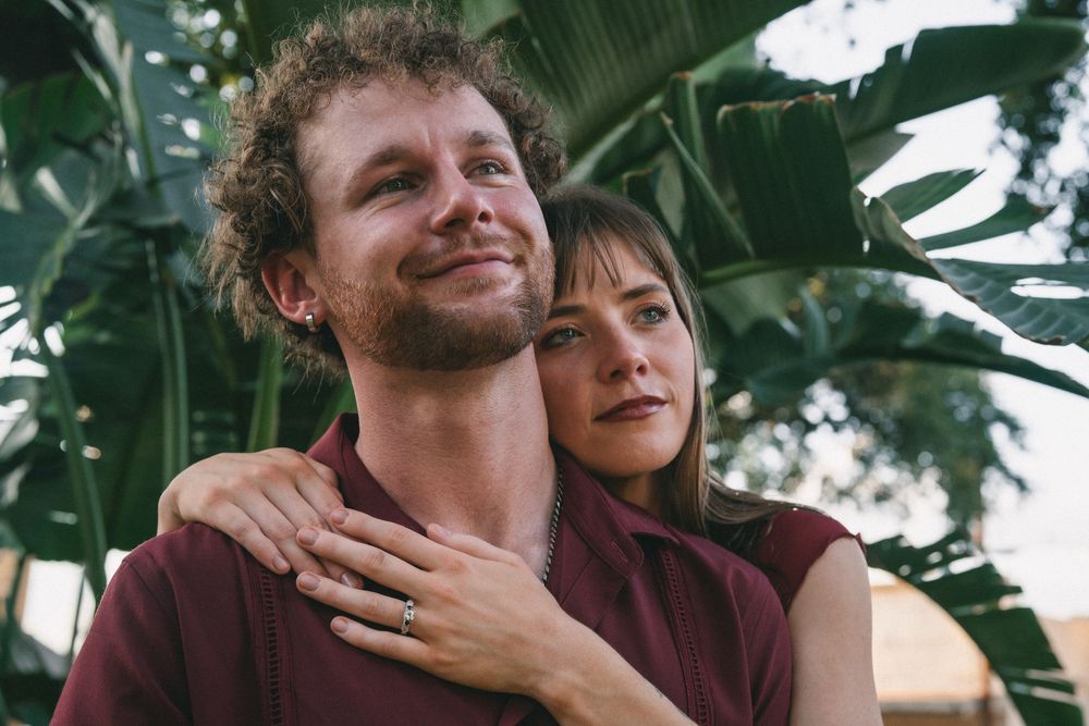 A couple shares joyful moments together against a backdrop of tropical plants.