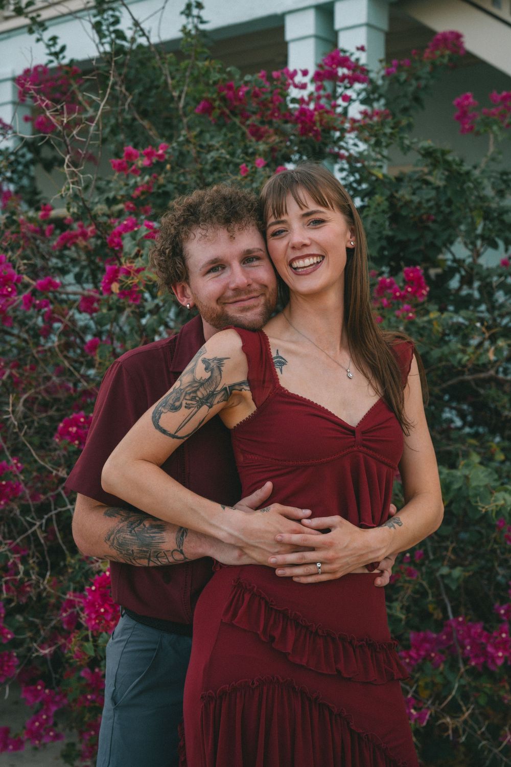 A couple embraces outdoors against a backdrop of vibrant pink bougainvillea flowers.
