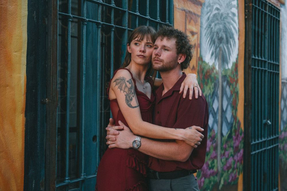 A couple poses together against a yellow wall with ornate iron bars.
