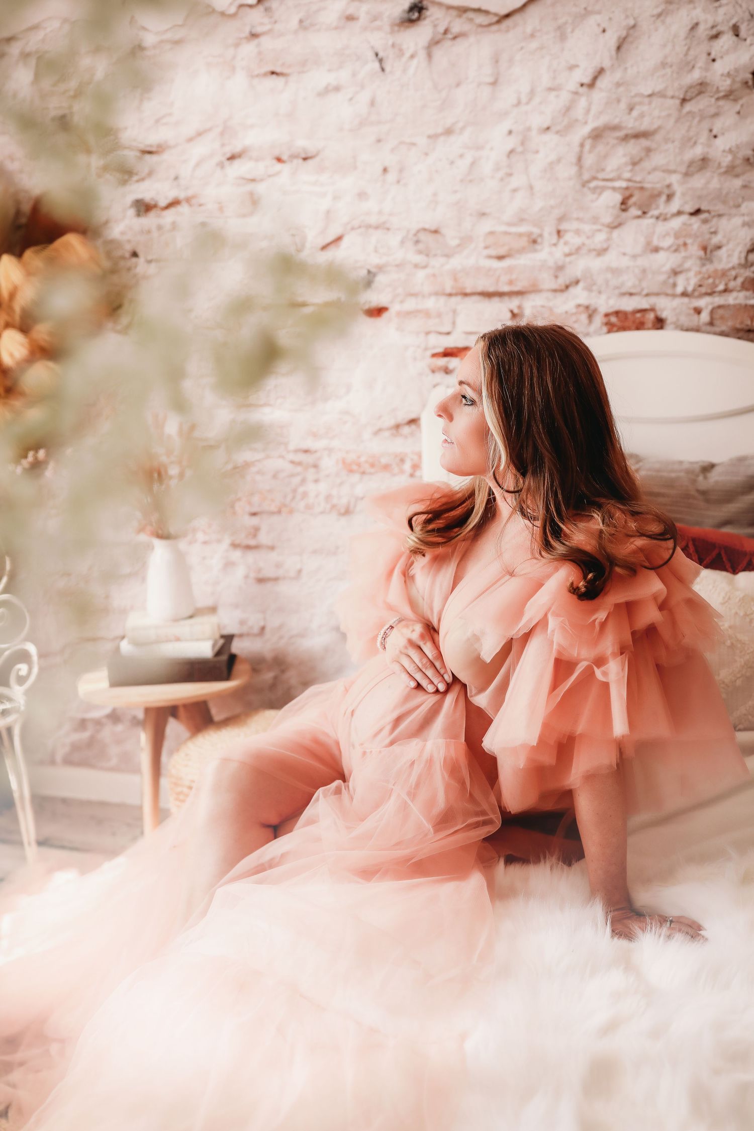 A person in a flowing peach-colored dress creates dreamy movement poses against a white brick wall background.
