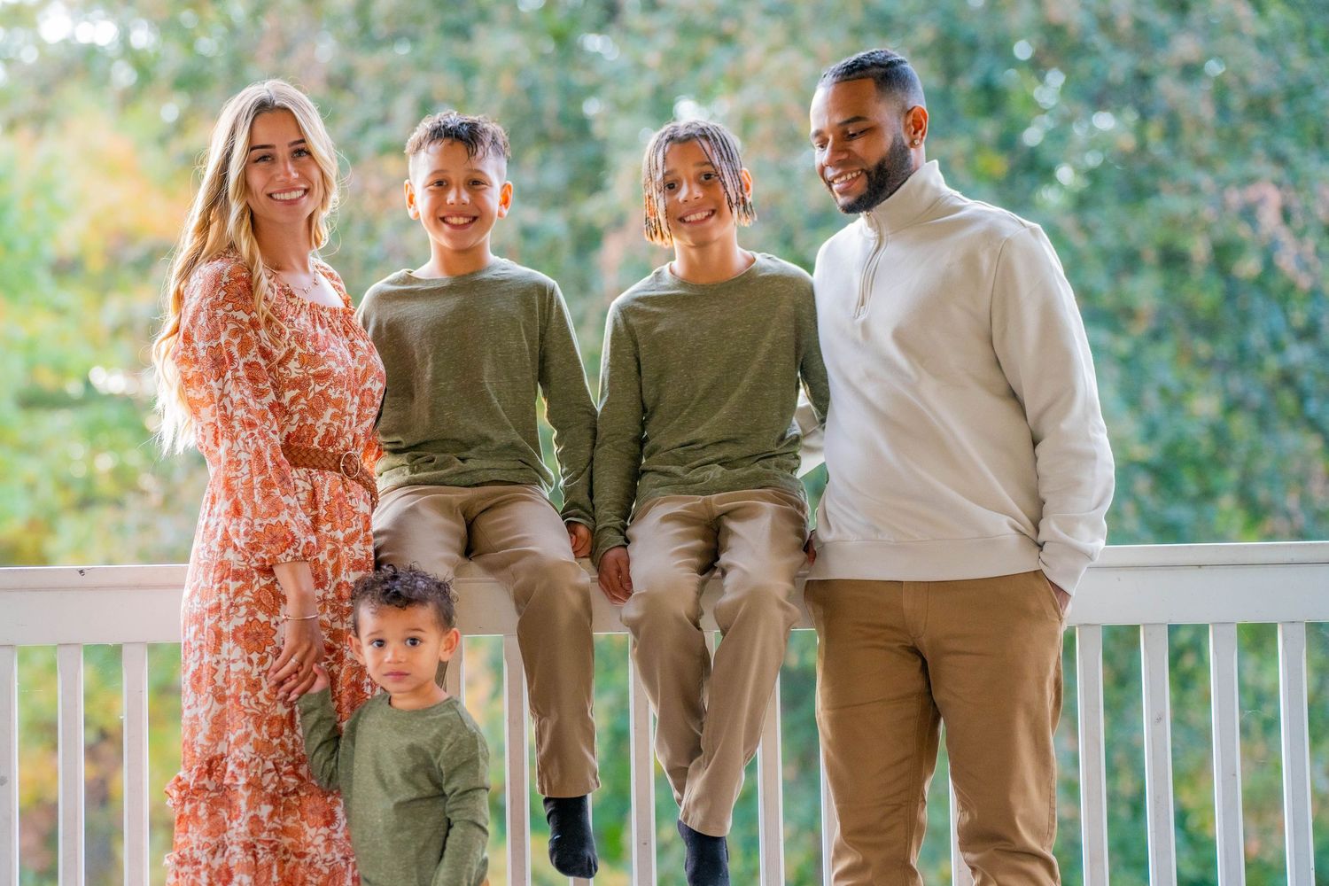 Family group photo on a porch wearing coordinated neutral tones and floral dress.