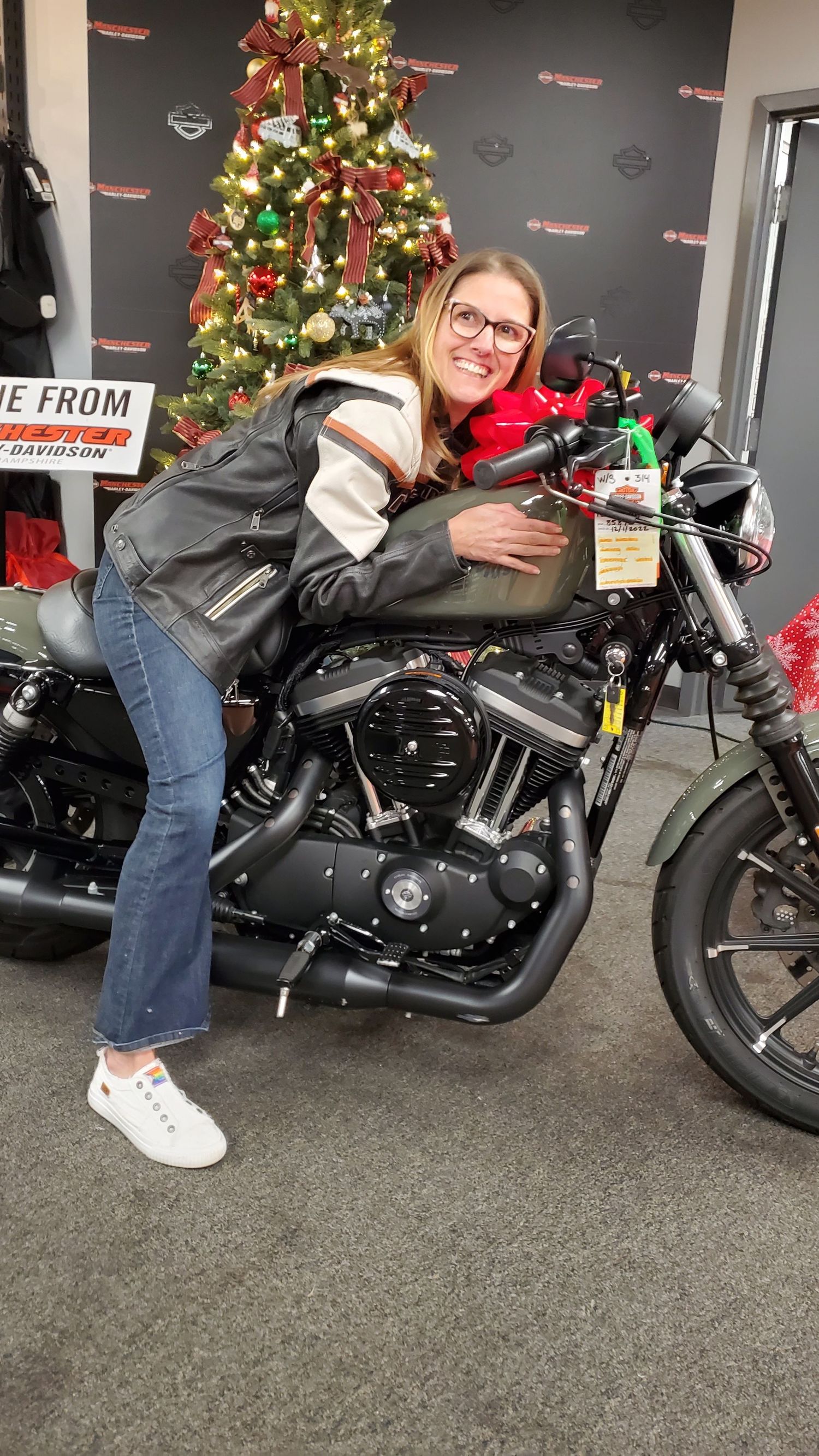 Person posing with a black motorcycle next to a decorated Christmas tree in a showroom.