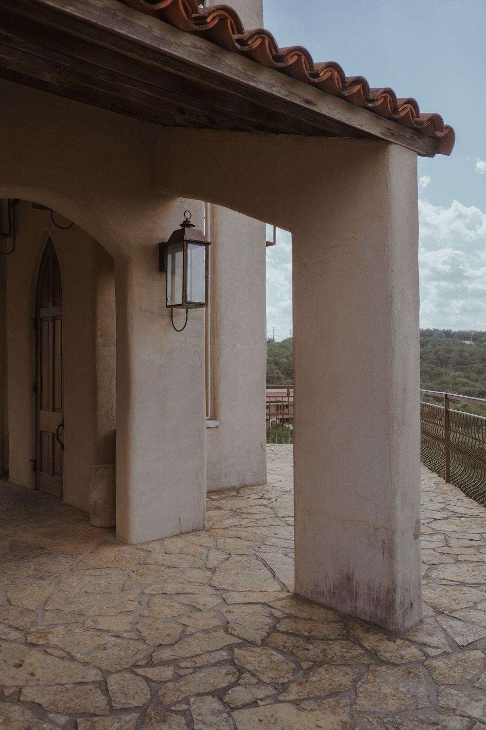 Stone patio with white stucco walls and Spanish tile roof creates a covered outdoor walkway at a Mediterranean villa.