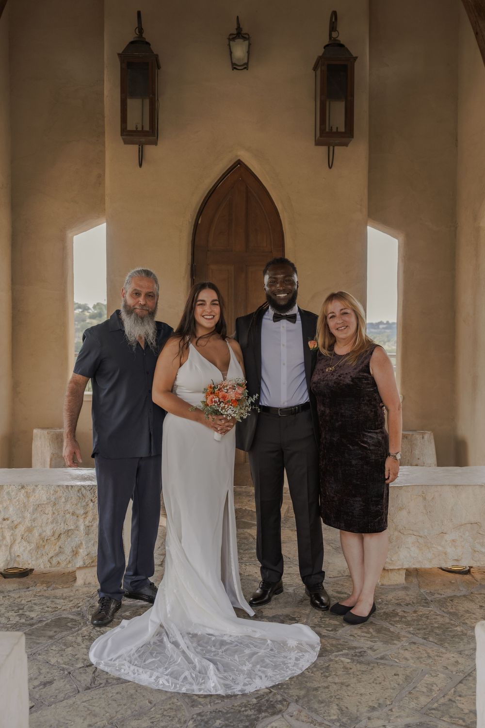 Wedding party gathered in a Spanish-style chapel with stone floors and arched windows.