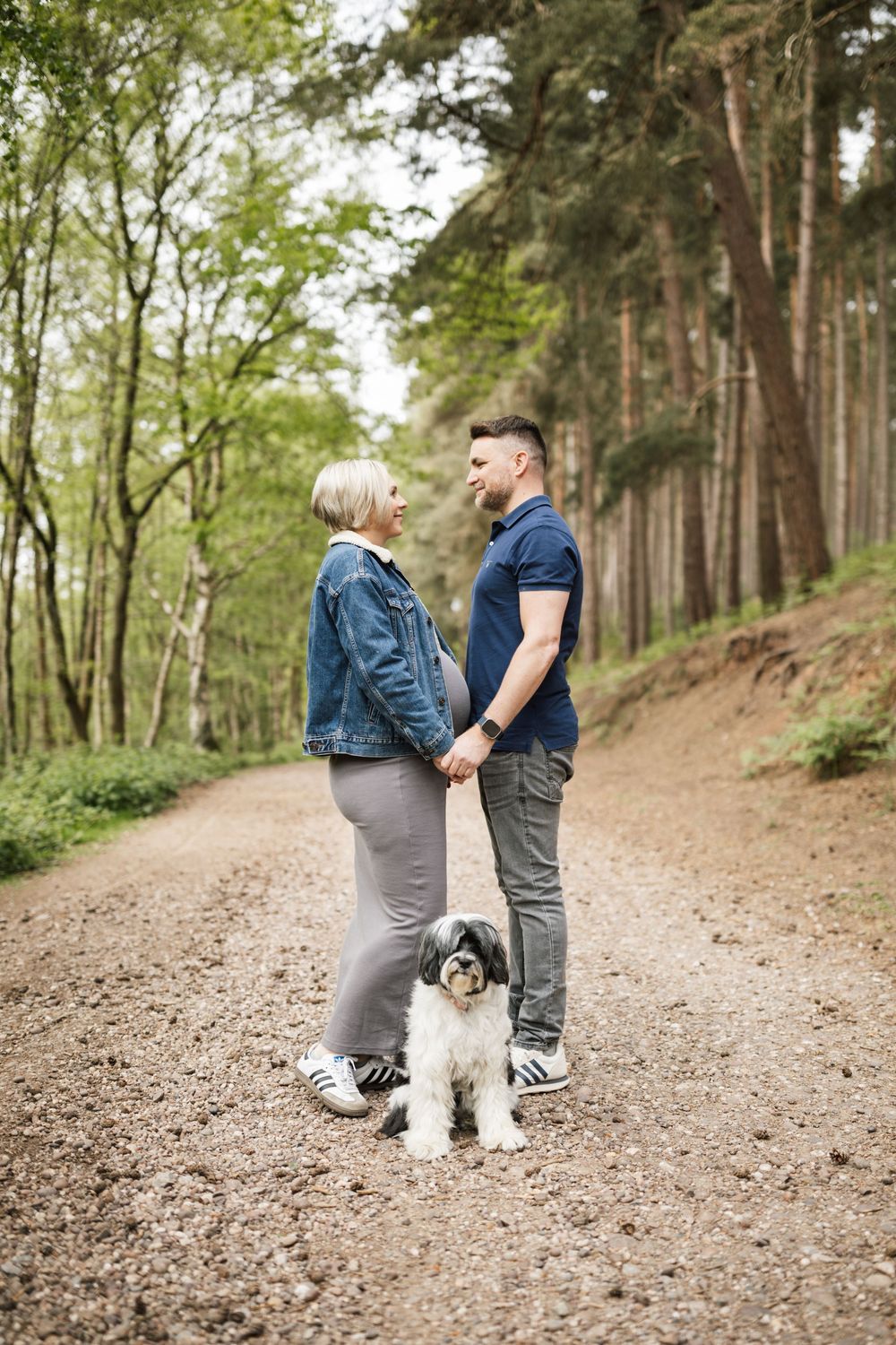 A couple walks along a wooded trail with their black and white dog on a peaceful autumn day.