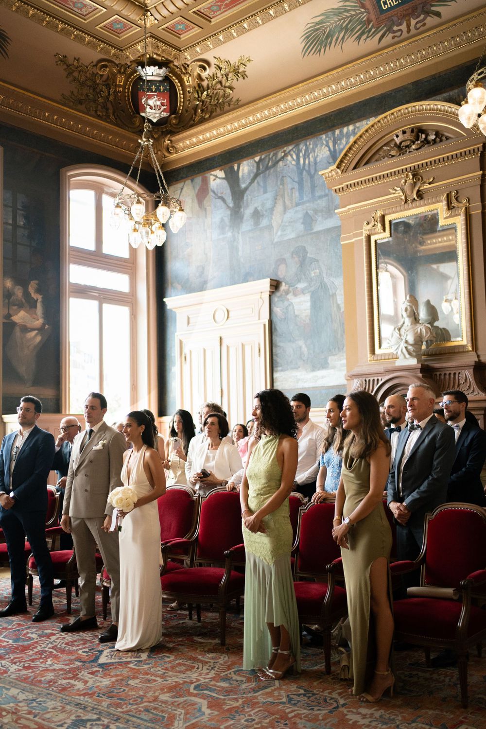 Guests standing in an ornate wedding ceremony hall with red chairs, murals, and gilded ceiling decor. Paris civil ceremony wedding photograp