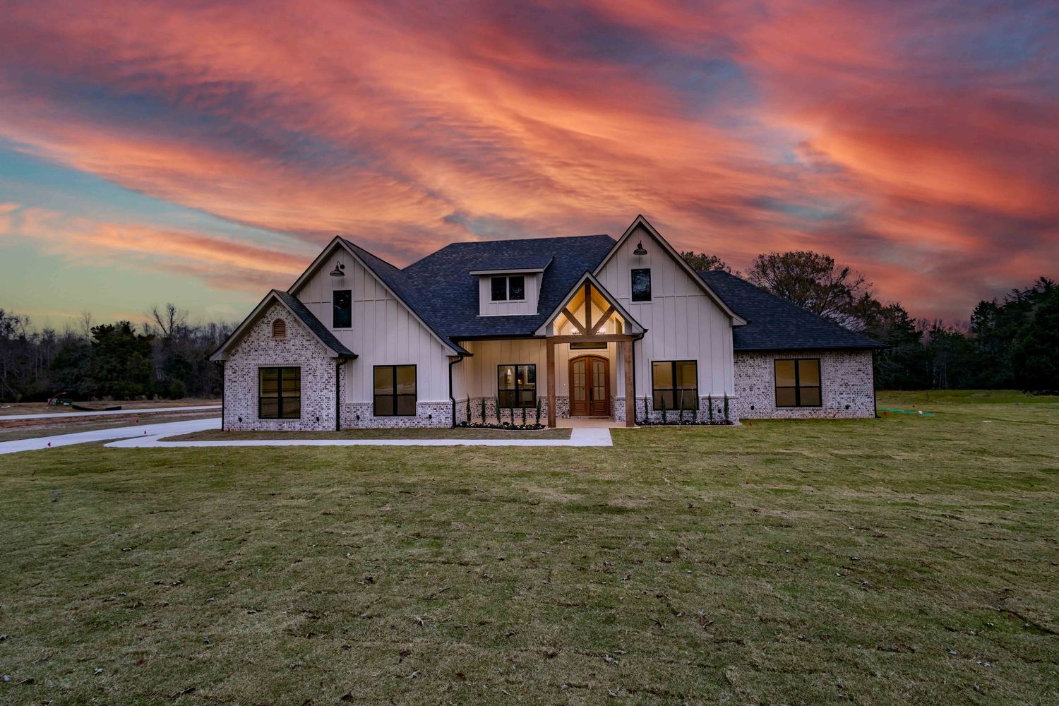 A modern white craftsman style house with a front porch and curved driveway surrounded by green lawn.
