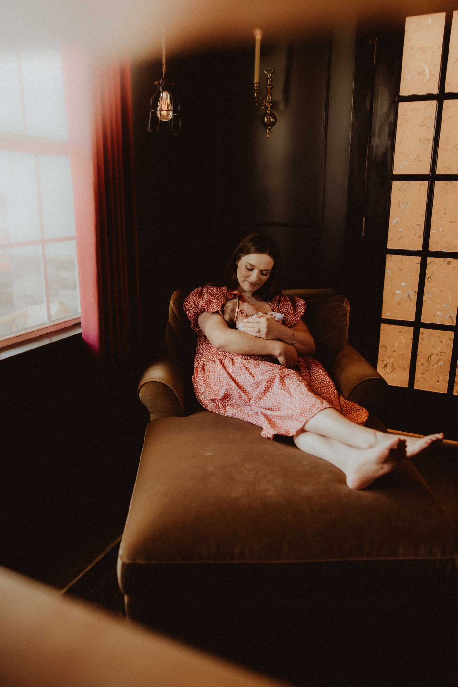 A figure in a pink dress lies gracefully across a dark couch in moody, atmospheric lighting.