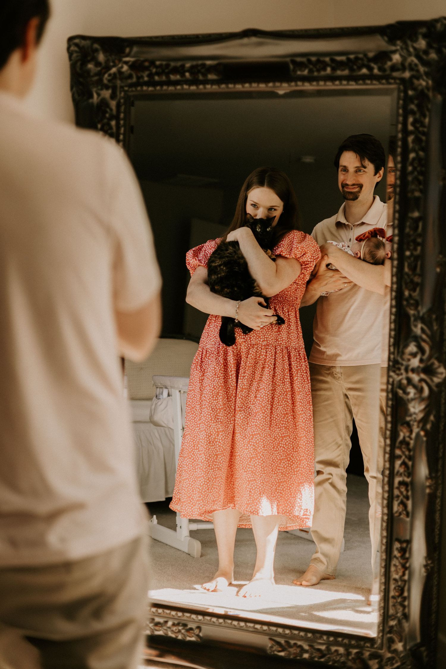 Mirror reflection shows a couple holding matching coral-colored dresses in a vintage-style interior setting.