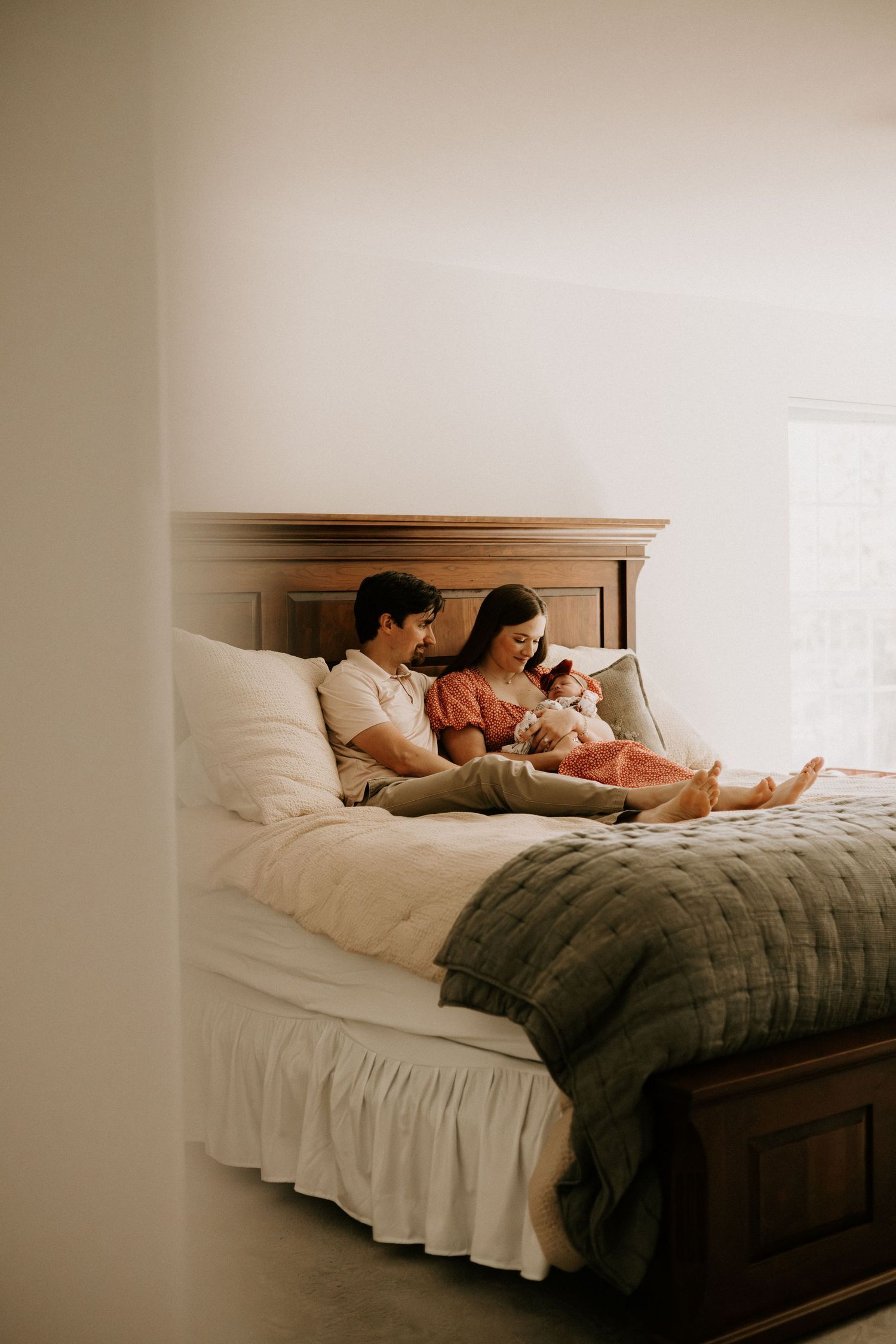 Family relaxes together on bed with newborn baby in cozy bedroom with warm lighting.