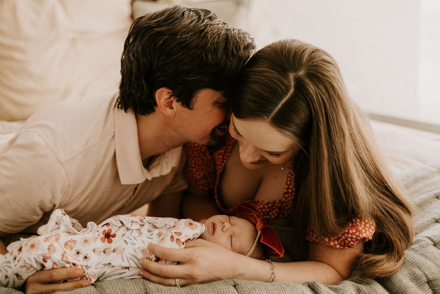 Two parents share an intimate moment with their newborn baby while laying together on a bed.