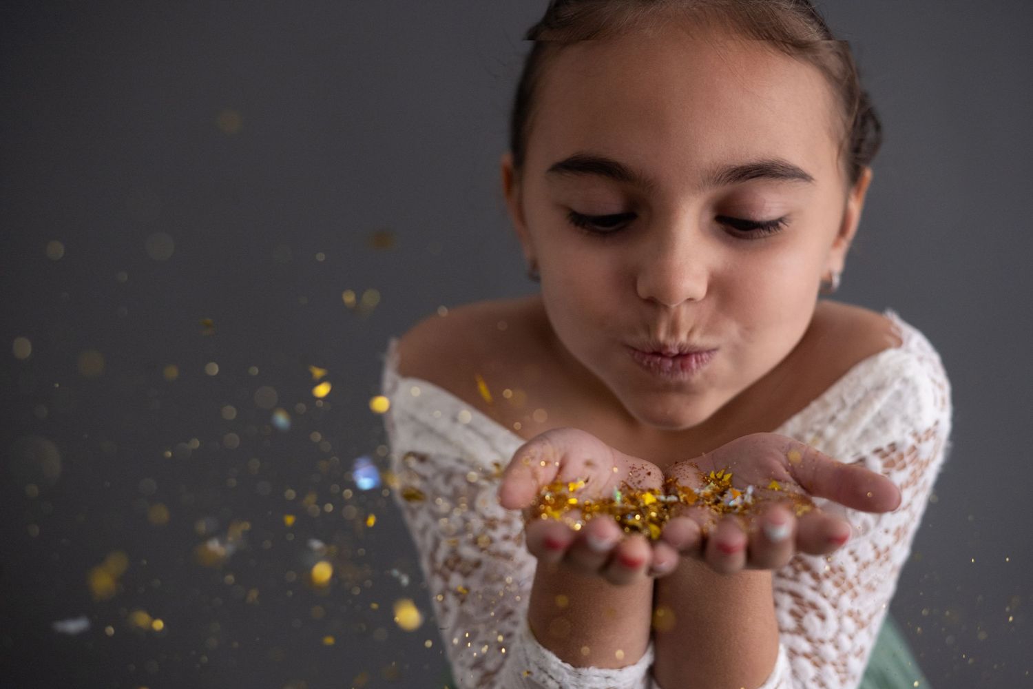 Person in white lace dress blowing gold glitter confetti in a dreamy photoshoot sequence.