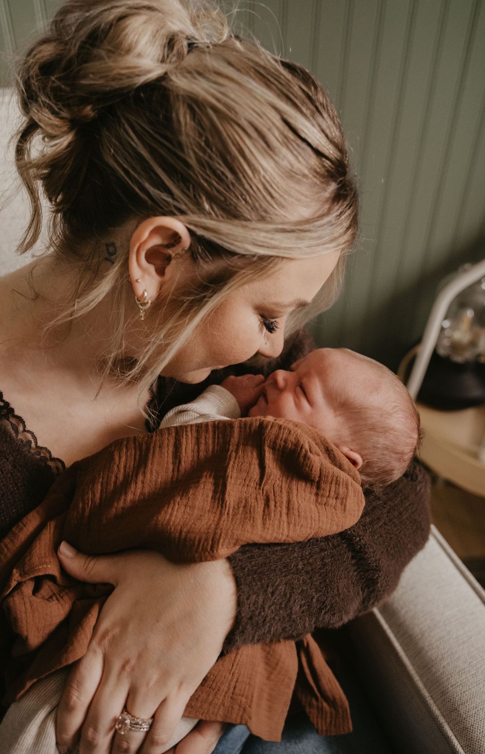 A tender moment captured between parent and newborn baby in warm brown tones by a window.