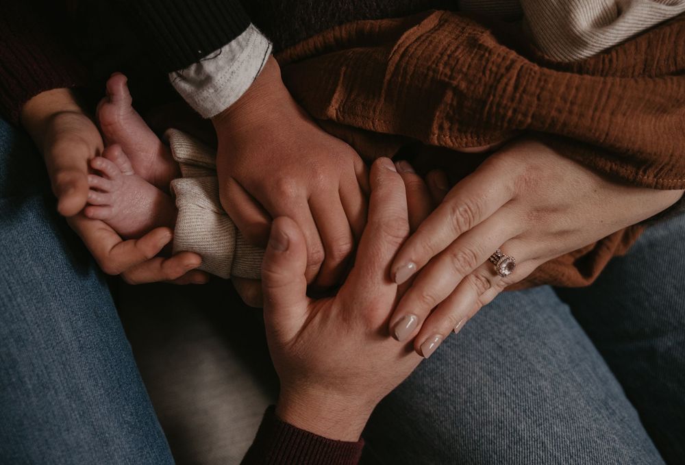 Multiple hands gently touching and holding each other against denim jeans in an intimate moment.