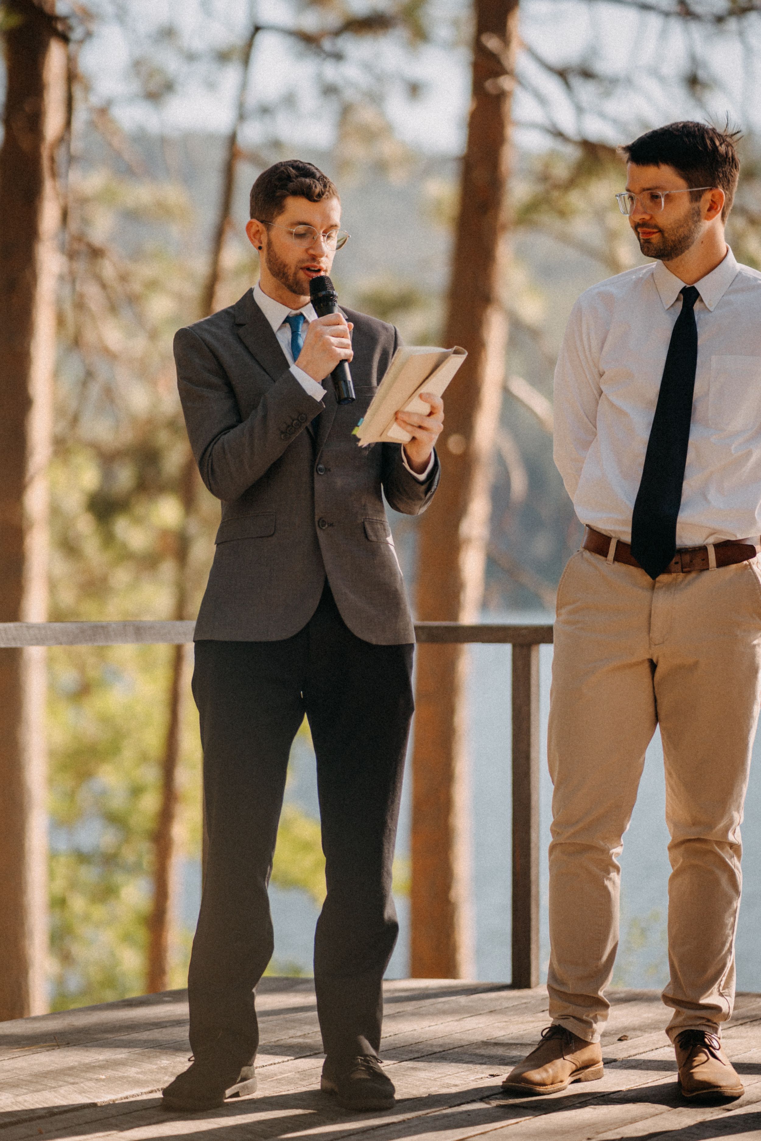 Groomsmen in suits and ties gather on a wooden deck surrounded by pine trees.