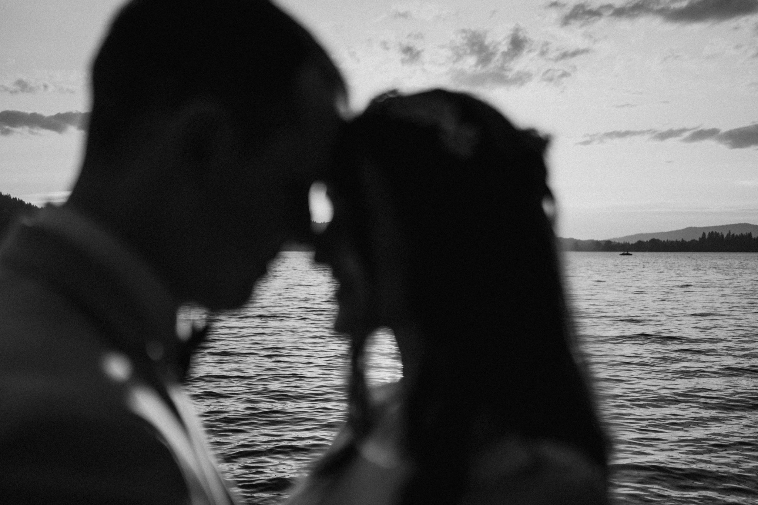 Silhouetted couple sharing an intimate moment against a sunset over water.