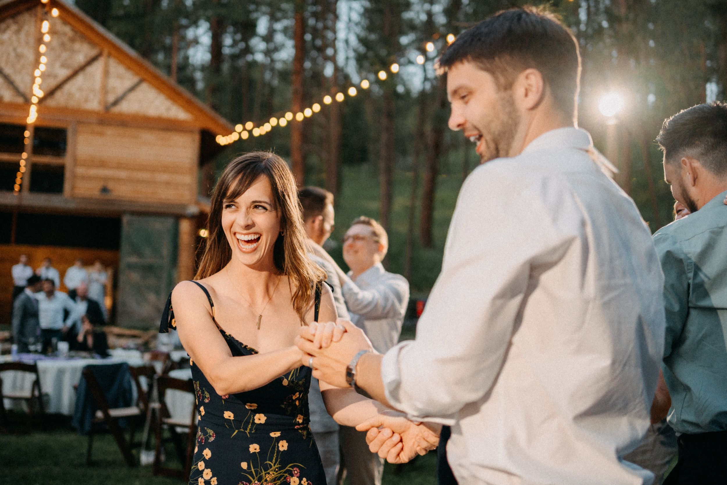 Wedding guests dance and celebrate under string lights at an outdoor rustic venue during evening reception.